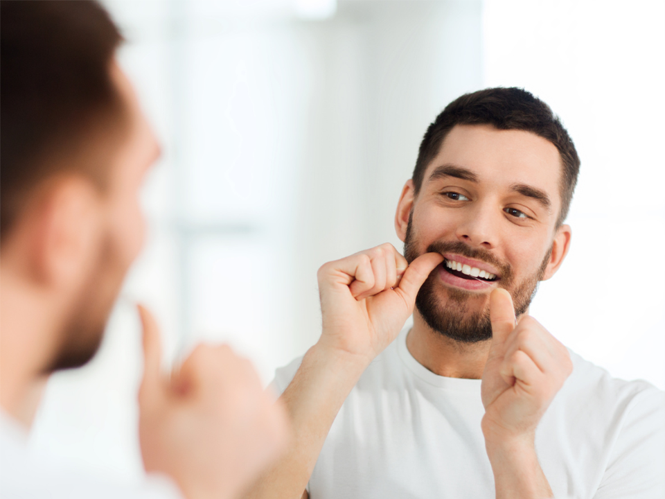 Man flossing his teeth in a mirror